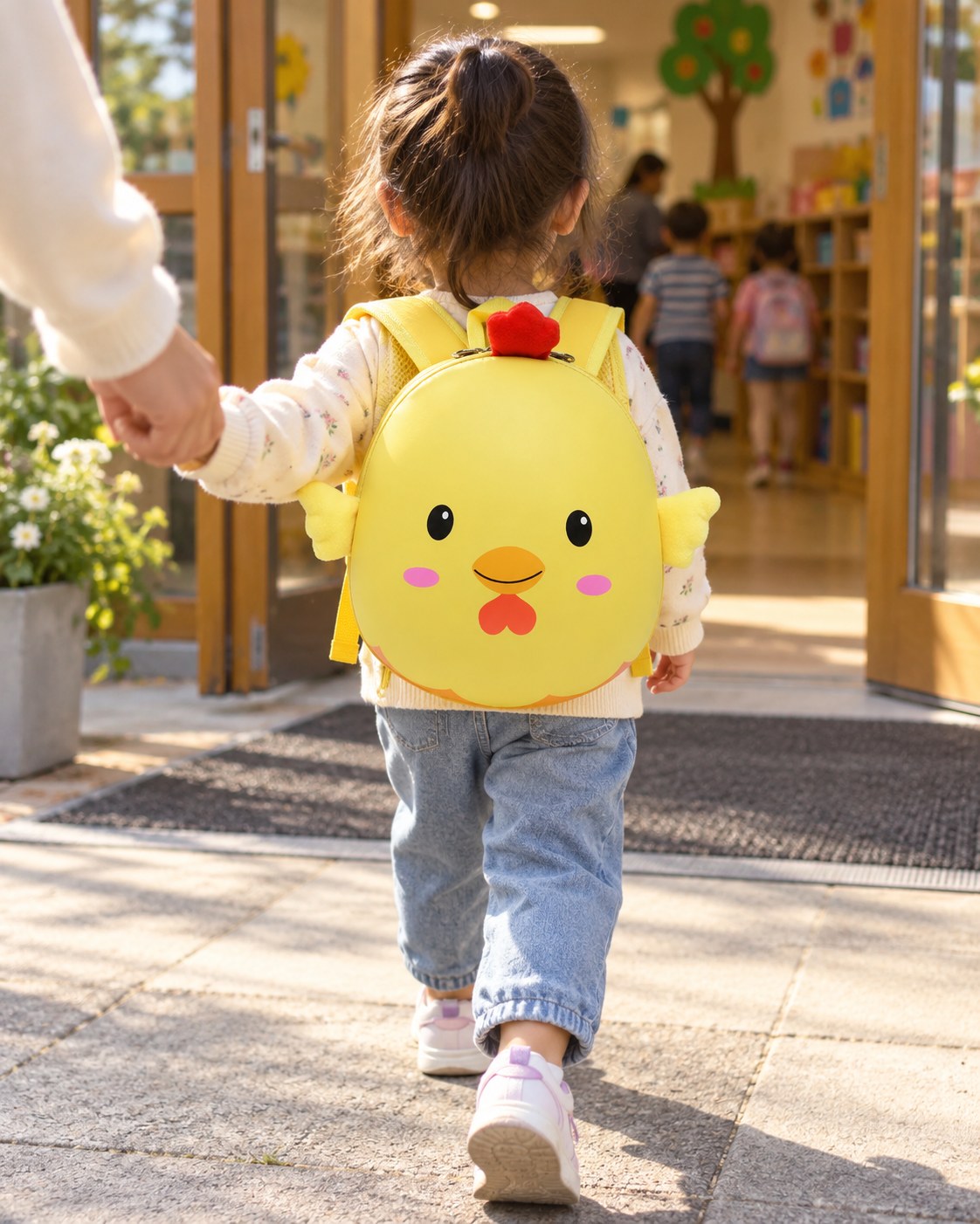 A child wearing a yellow chick backpack at a school entrance