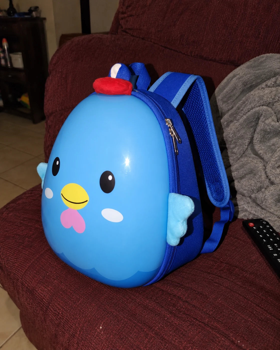 Illustrative right-side phone-style photo of the blue chick backpack on a sofa